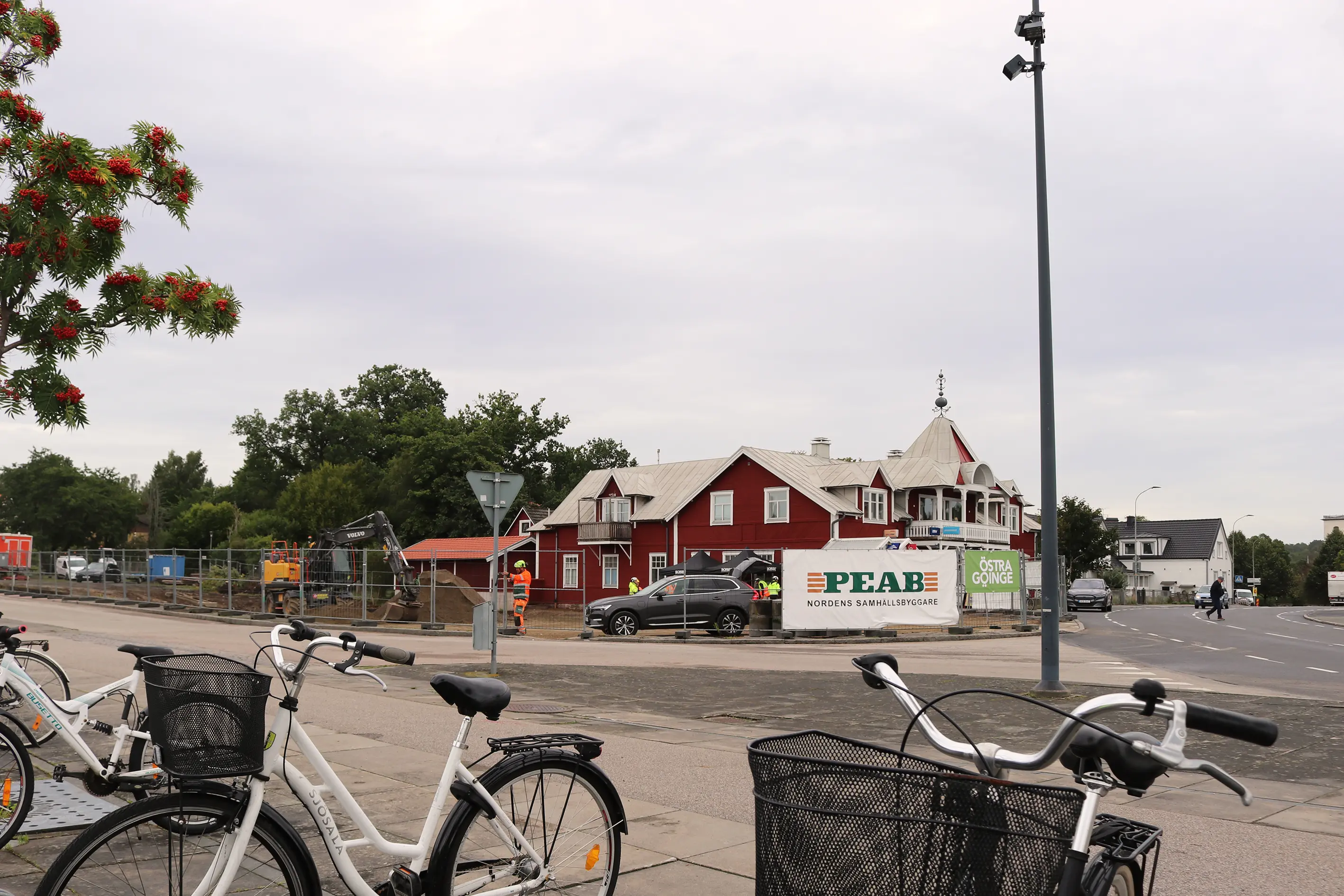 Bild med cyklar i förgrunden och en byggarbetsplats med stängsel framför ett rött äldre hus i trä.